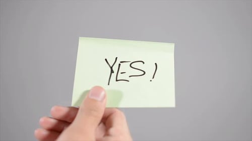 Hand Writes Yes on Light Green Sticky Note