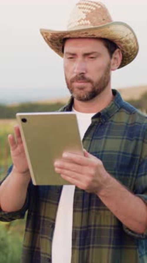 Bearded Man Farmer in Straw Hat Controls Using a Digital Tablet to Access Modern Technologies and