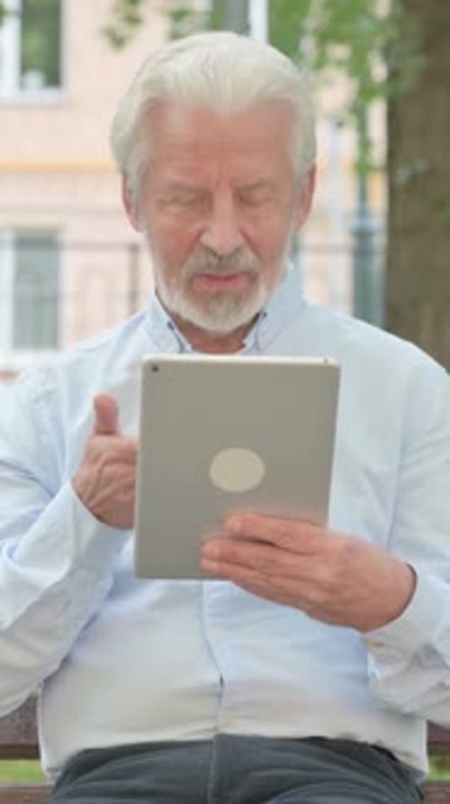 Senior Old Man Doing Video Chat on Tablet while Sitting in Park, vertical video