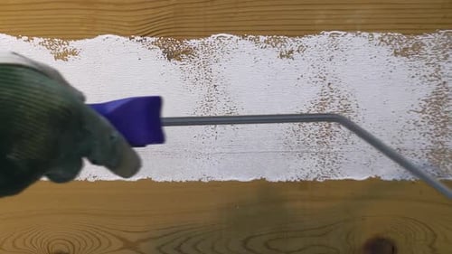 White Paint Roller Applies Paint to Wood Paneling