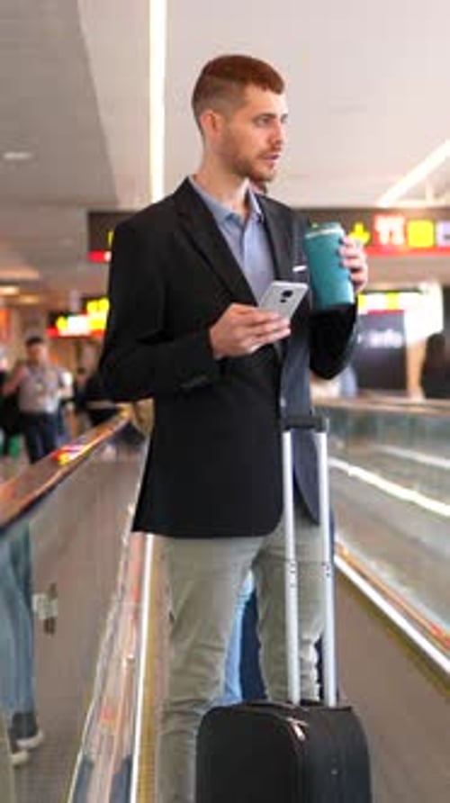Businessman using smartphone and drinking coffee at airport