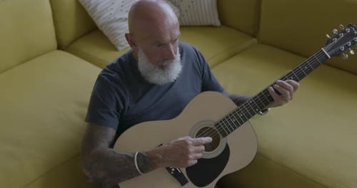 Senior Man Plays Acoustic Guitar on Couch