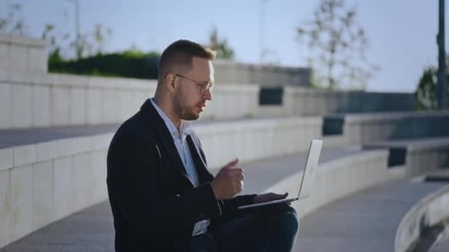 A Businessman Conducts a Video Conference Via a Laptop While Sitting on the Street Urban Spaces are