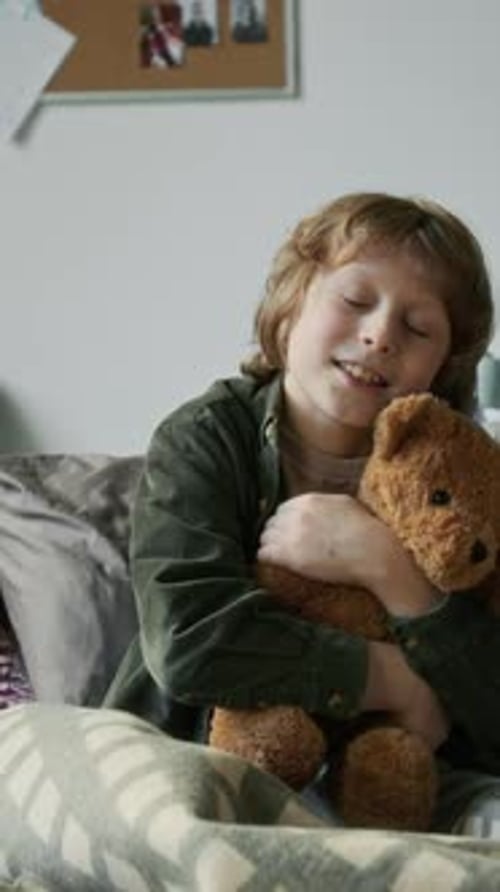 Portrait of Smiling Caucasian Refugee Boy Hugging Teddy Bear in Shelter