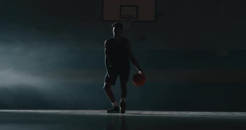 Young Adult Dribbles Basketball on Dark Indoor Court