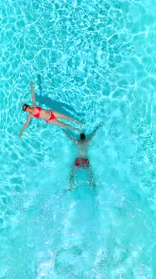 Top Down View As a Man Dives Into the Pool While Woman is Laying on Her Back