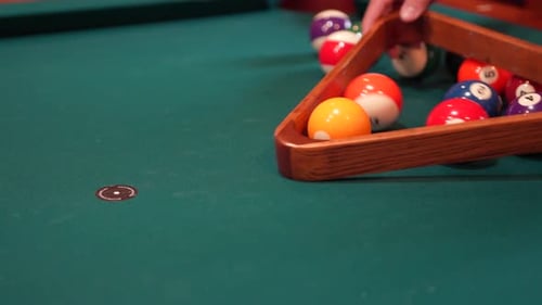 Person Racks 8 Ball Pool Triangle Closeup on the Spot gathering Solid and Stripped Billiard Balls on