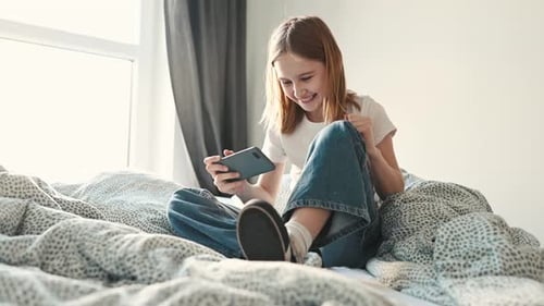 Smiling Girl Using Smartphone on Bed at Home