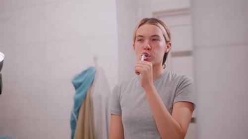 Woman Brushing Teeth in Tiled Bathroom Mirror