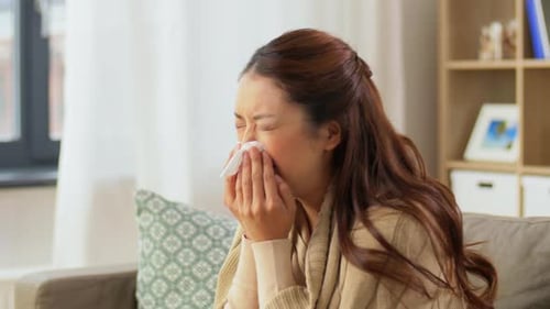Woman with cold blowing her nose at home