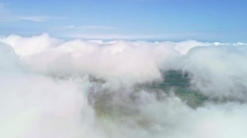 Descend Aerial drone flight through white clouds revealing green farm fields in the valley