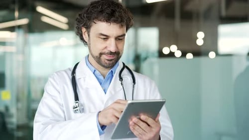 Mature doctor in white coat using digital tablet standing in modern hospital clinic. Medical worker