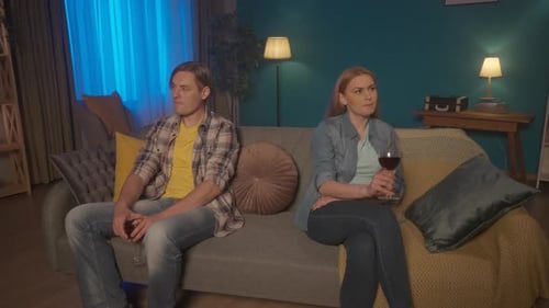 The Couple are Sitting on the Couch with Glasses of Red Wine Facing Away From Each Other A Man and a