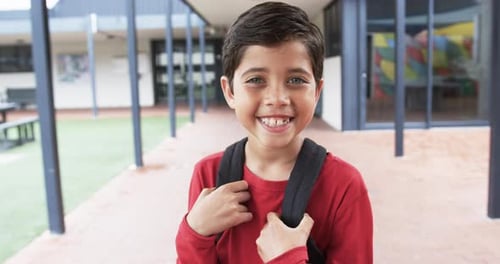 In a school courtyard, a young Caucasian boy smiles brightly