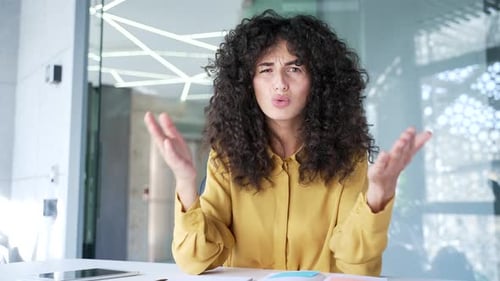 Webcam view. Angry female executive arguing on video call looking at camera sitting at workplace