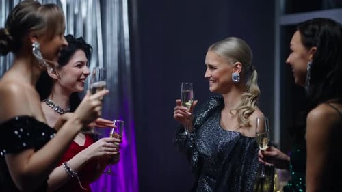 Felizes mulheres lindas tilintando óculos e sorrindo em um evento de gala de feliz noite de Natal à noite