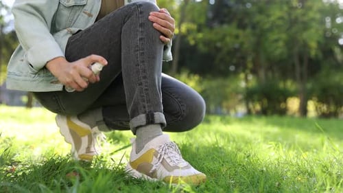 Woman spraying tick repellent onto leg in park, closeup