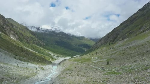 Drone flight over a winding glacier river through a high mountain alpine valley.