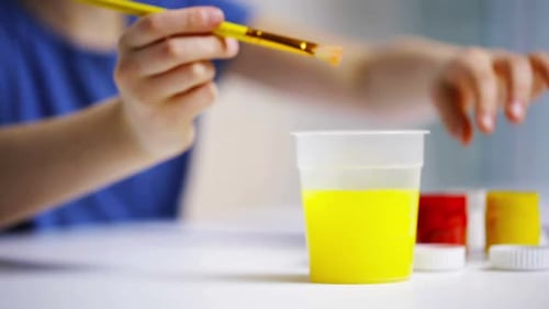 Girl dips paint brush in red paint for art