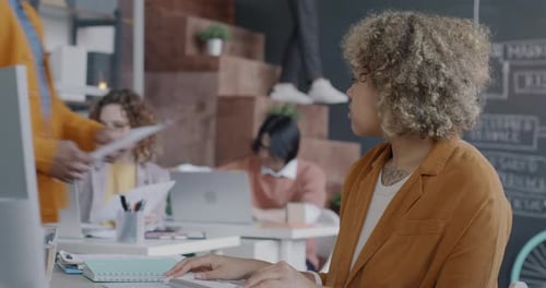 African American Woman Office Employee Working with Computer Typing Getting Document From Male