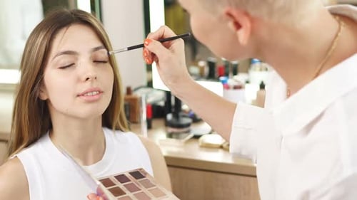 Makeup Artist Applying Eyeshadow to Young Adult Woman