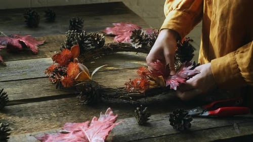 Woman crafting autumn wreath from pine cones and leaves