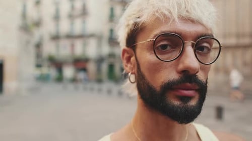Close up, handsome guy with blond hair wearing glasses crosses his arms and looks at camera