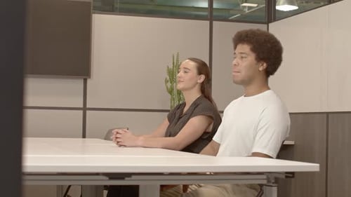 African American male in his 20's and a caucasian female in her 20's talking in business meeting wit