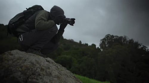 Man Squats Taking Pictures of Overcast Mountain Landscape
