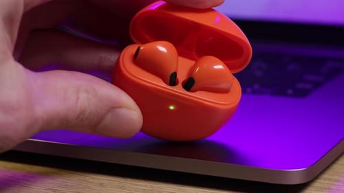 Finger Opens Orange Earbud Case on Laptop