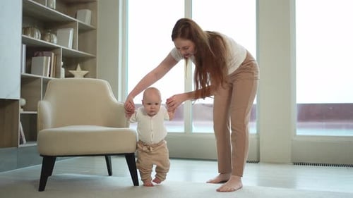 Mother helping infant learn to walk in home