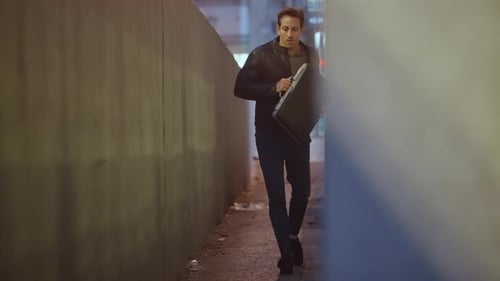 Un homme tenant une mallette s'enfuit dans une ruelle urbaine sombre de la ville, l'air effrayé. Inquiet et méfiant