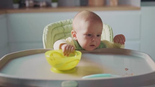 Infant Plays with Bowl in High Chair