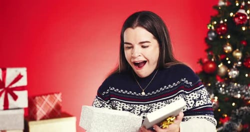 Surprise woman, face and christmas with gift box in studio for giving or offer on a red background