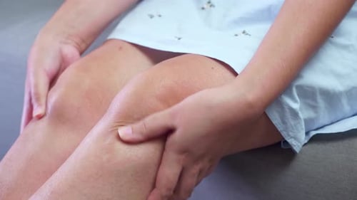 Close-up of an individual squeezing, pressing, and pinching her knees to relieve the swelling and in