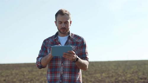 Smiling Man Farmer Holding a Tablet Studying Harvest on the Rural Field in Sunny Weather Cheerful