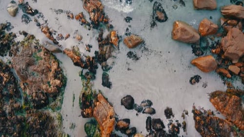 Vista aérea desde arriba de las olas del océano Atlántico chocando contra hermosas rocas naturales de color marrón rojizo con algas