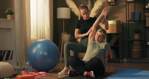 Trainer Assists Woman Stretching Arm at Home