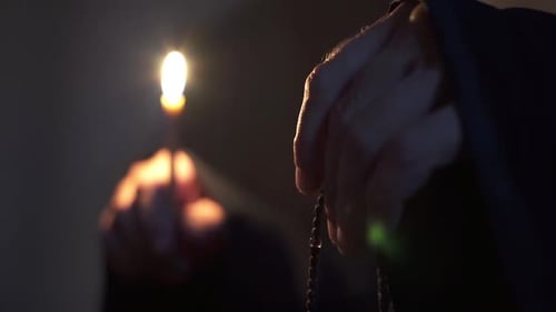 Hands Holding Rosary and Candle in Dark