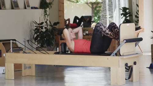 Fit senior caucasian woman stretching on reformer in pilates studio, unaltered, in slow motion