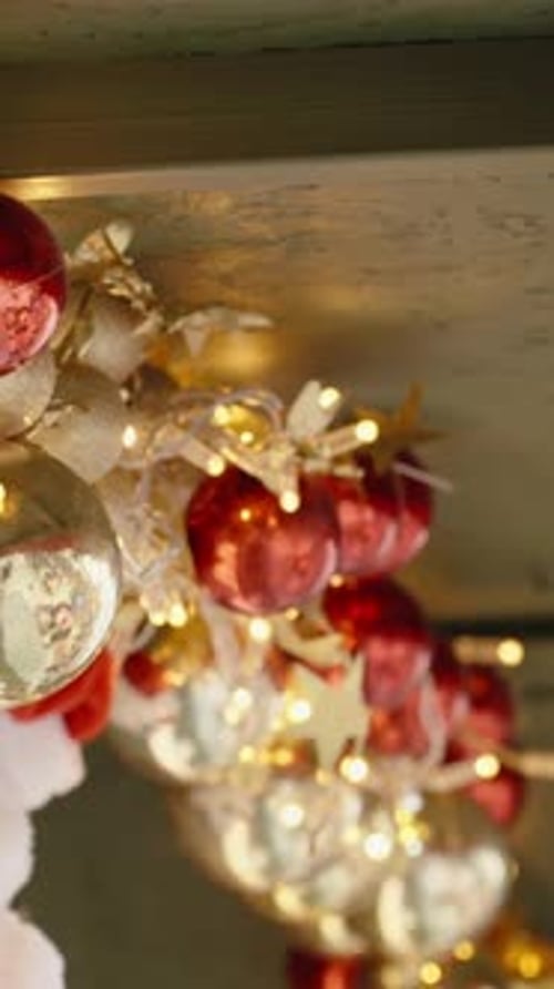 Vertical video. Gold and red Christmas tree ornaments hang on the eaves of the wooden house. Close-u