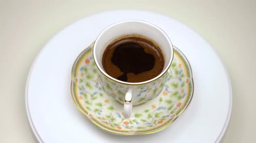 Rotating old-fashioned coffee mug with flowers. White background.