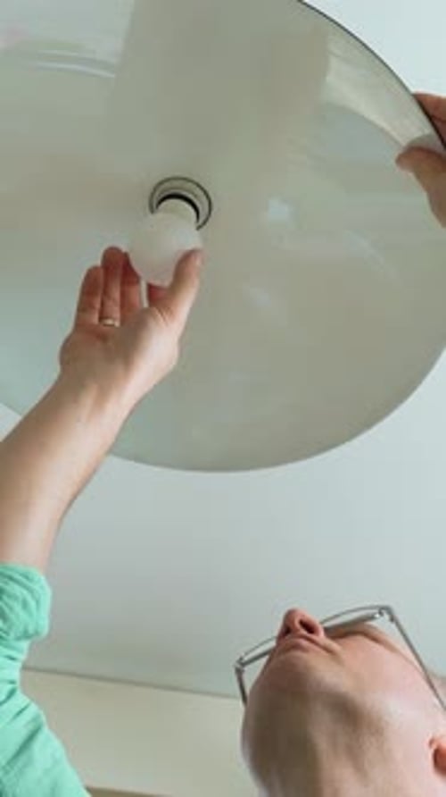 Hombre de mediana edad cambia bombilla de bajo consumo y lámpara de techo