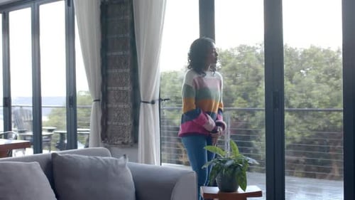 Thoughtful biracial woman looking through window at home, slow motion, copy space