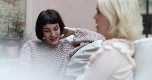 Two Women Conversing on Couch in Home Setting