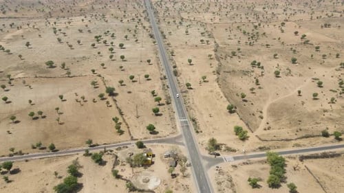 Aerial drone shot showing a car moving through a desolate desert highway with distant dunes.