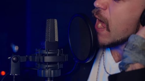 Nahaufnahme des Gesichts eines professionellen Sängers und eines Mikrofons im Aufnahmestudio bei der Aufnahme eines neuen Songs
