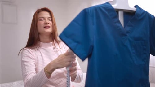 Woman Steaming Blue Scrubs in Bedroom