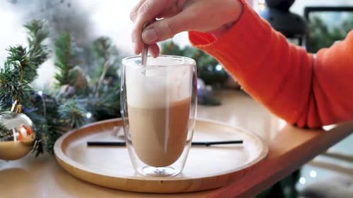 Closeup of the Hands of a Woman Who is Stirring Coffee with a Spoon in a Transparent Mug in a Cafe