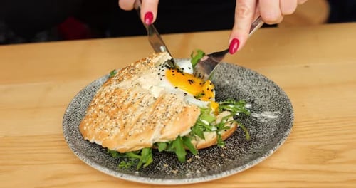 Woman Hands Eat City Breakfast Cut Runny Yolk of Fried Egg with Fork and Knife